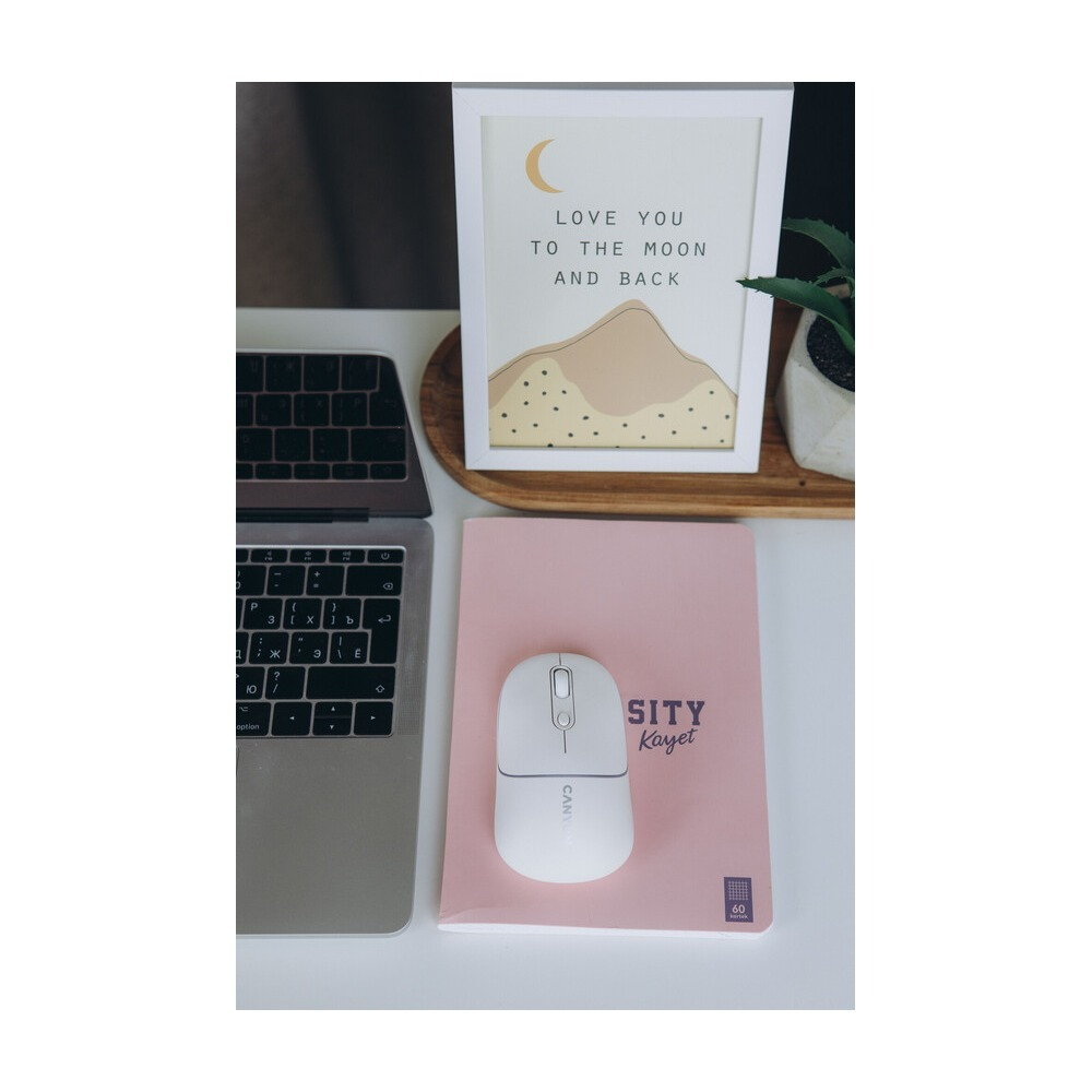 Laptop, myszka na różowym notesie oraz oprawiony obraz z napisem Love you to the moon.