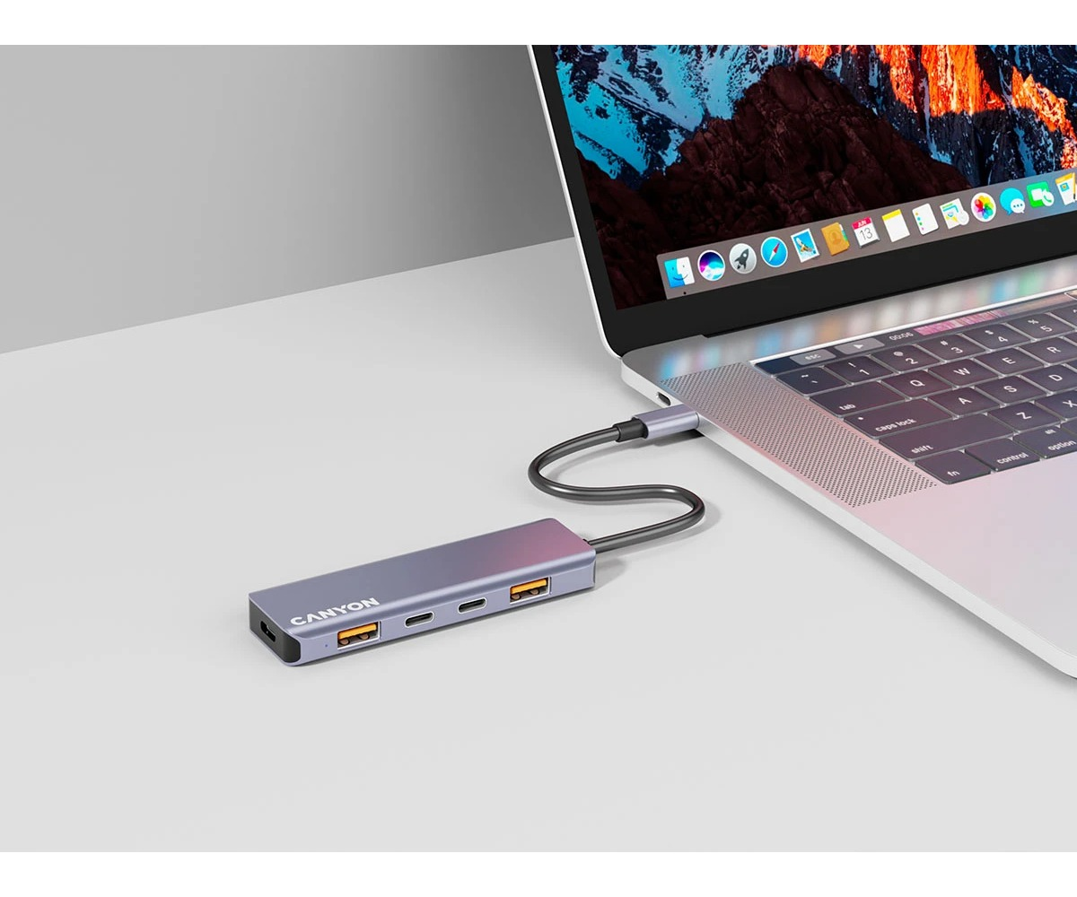 Szary hub wieloportowy USB-C Canyon jest podłączony do srebrnego laptopa na białym biurku.