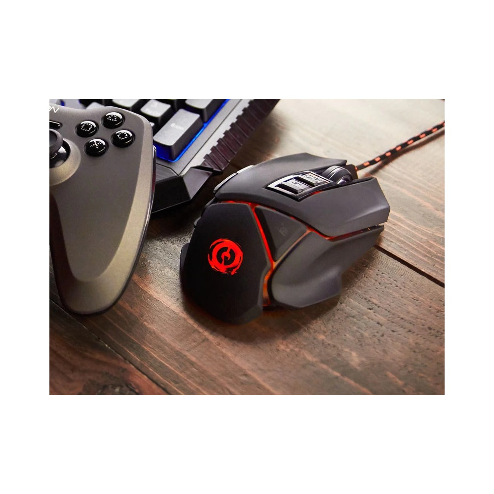 Un ratón de juego negro con luz LED roja, un mando y un teclado en una mesa de madera.