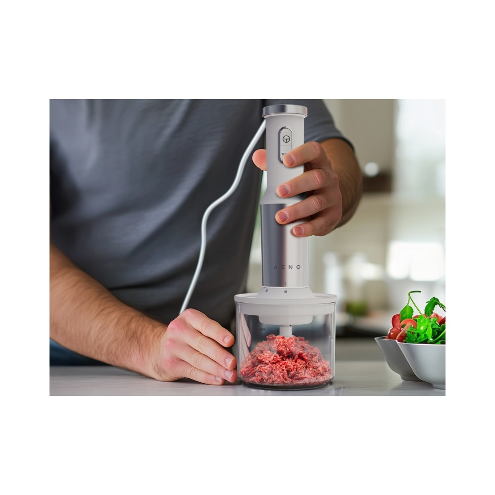 Osoba trzymająca blender ręczny siekający mięso mielone w przezroczystym pojemniku.