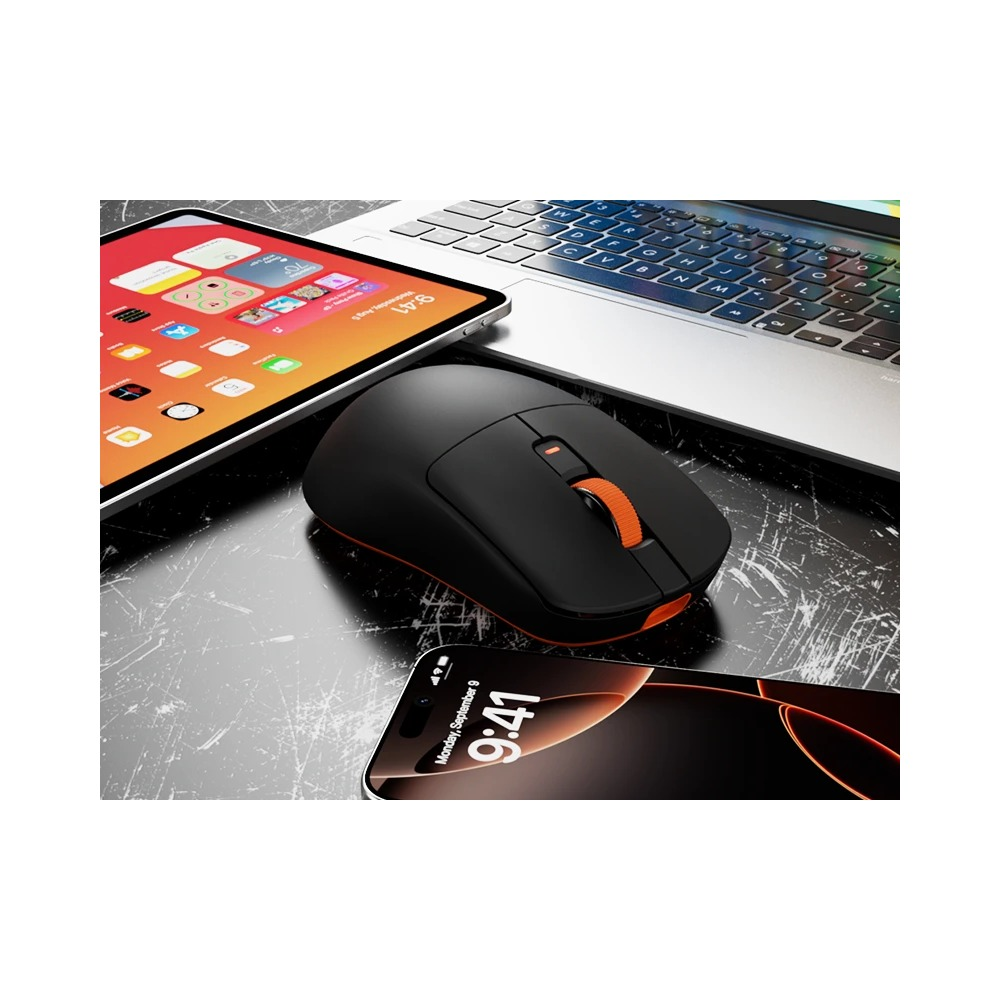 Czarna mysz komputerowa z pomarańczową rolką obok laptopa, tabletu i smartfona na ciemnym biurku.