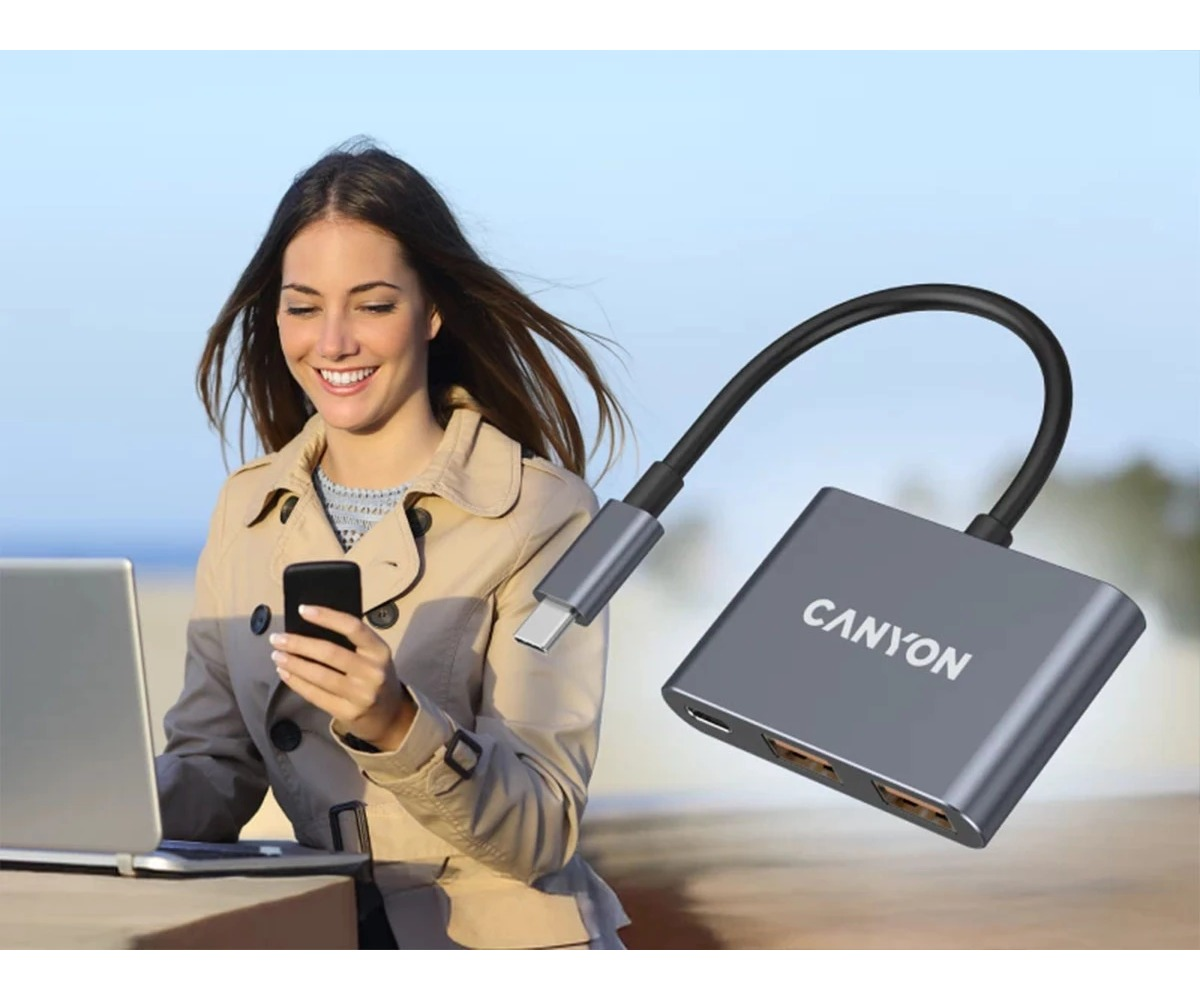 Uśmiechnięta kobieta korzysta z telefonu obok laptopa z hubem USB-C Canyon.