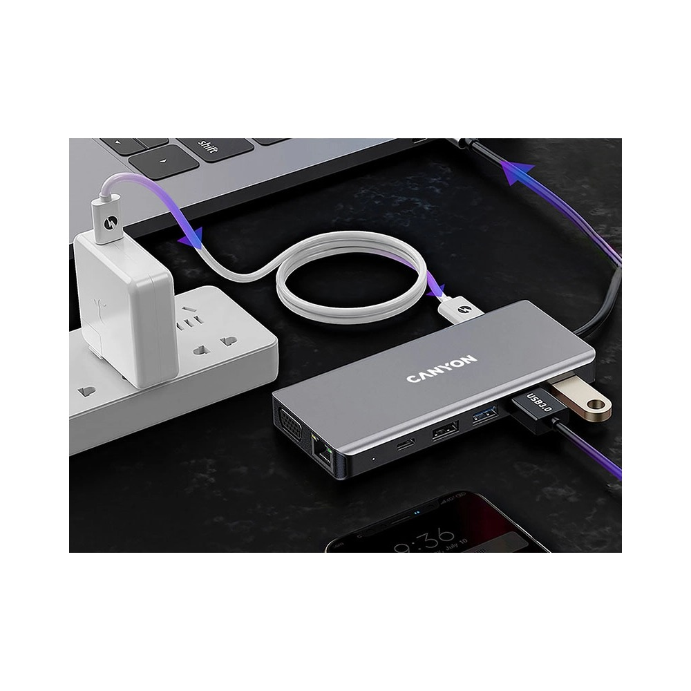 Szary hub USB-C Canyon podłączony do laptopa i kabli na ciemnej powierzchni.
