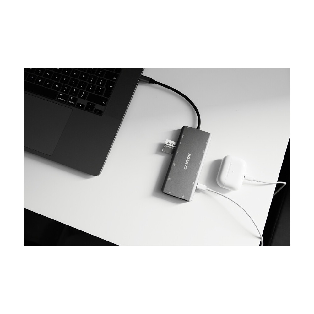 Szary hub USB-C Canyon z kartą SD na białym biurku obok laptopa i słuchawek.