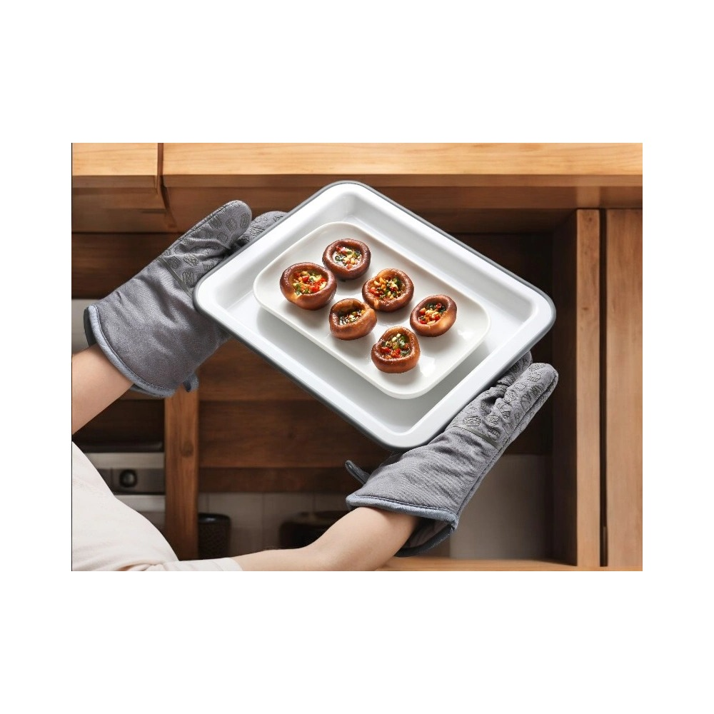 Persona con guanti da forno grigi tiene un vassoio di funghi ripieni in cucina.