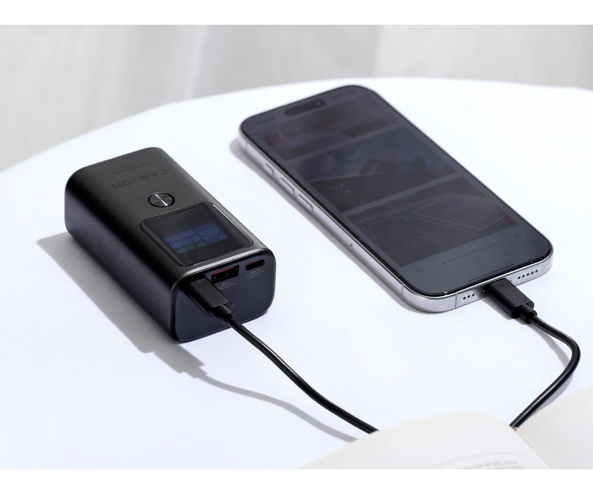Czarny powerbank i smartfon leżą na białej powierzchni, połączone kablem.