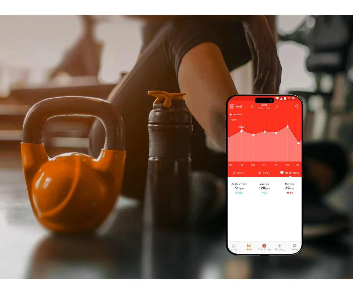 Pomarańczowy kettlebell i shaker leżą na podłodze obok smartfona z aplikacją fitness.