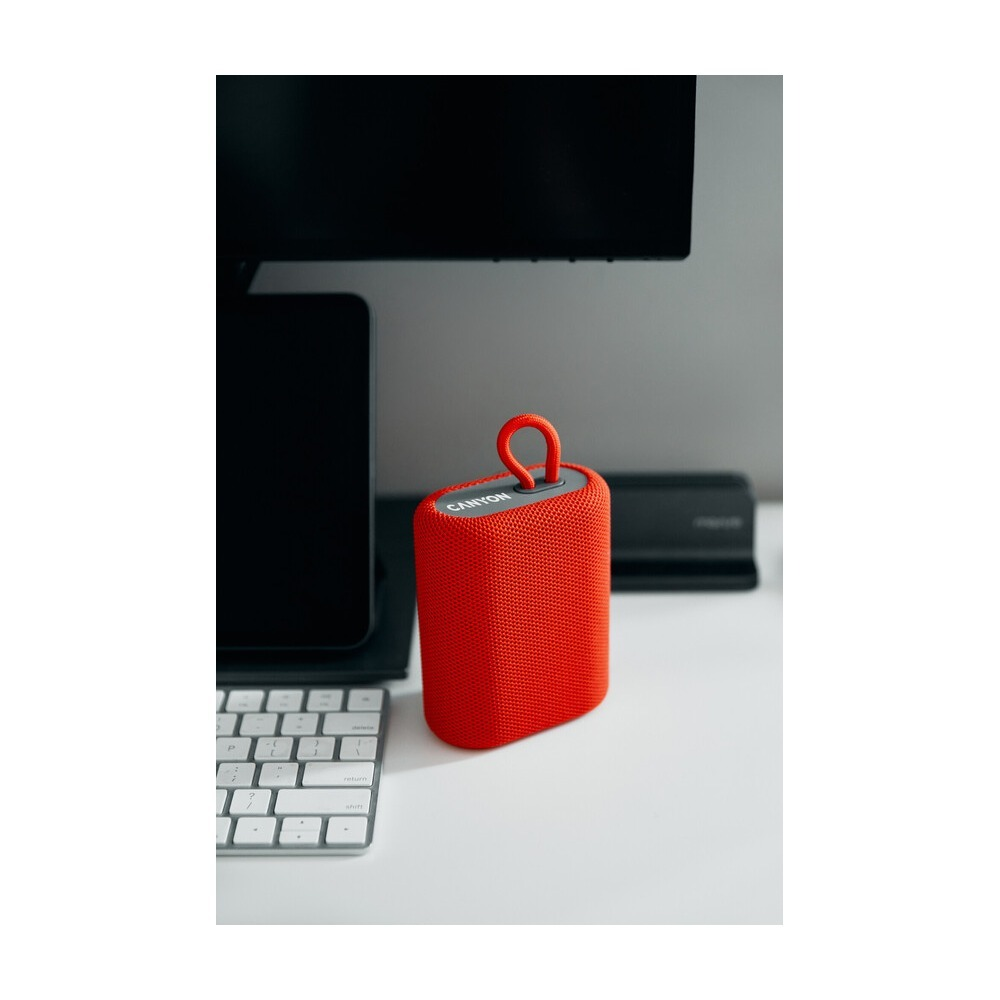 Czerwony głośnik Bluetooth Canyon stoi na białym biurku obok klawiatury i monitora.