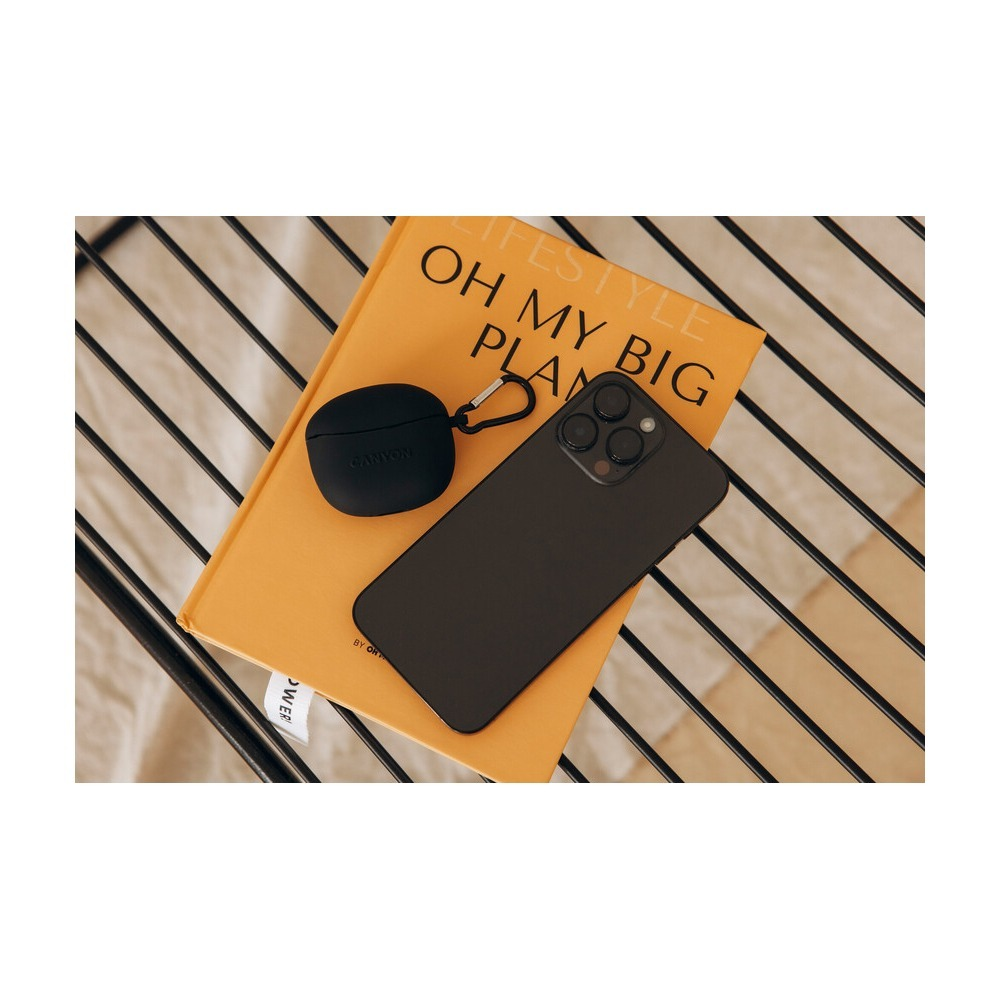 Ein schwarzes Smartphone und Kopfhörer in einem Case liegen auf einem gelben Buch auf einer gerippten Unterlage.