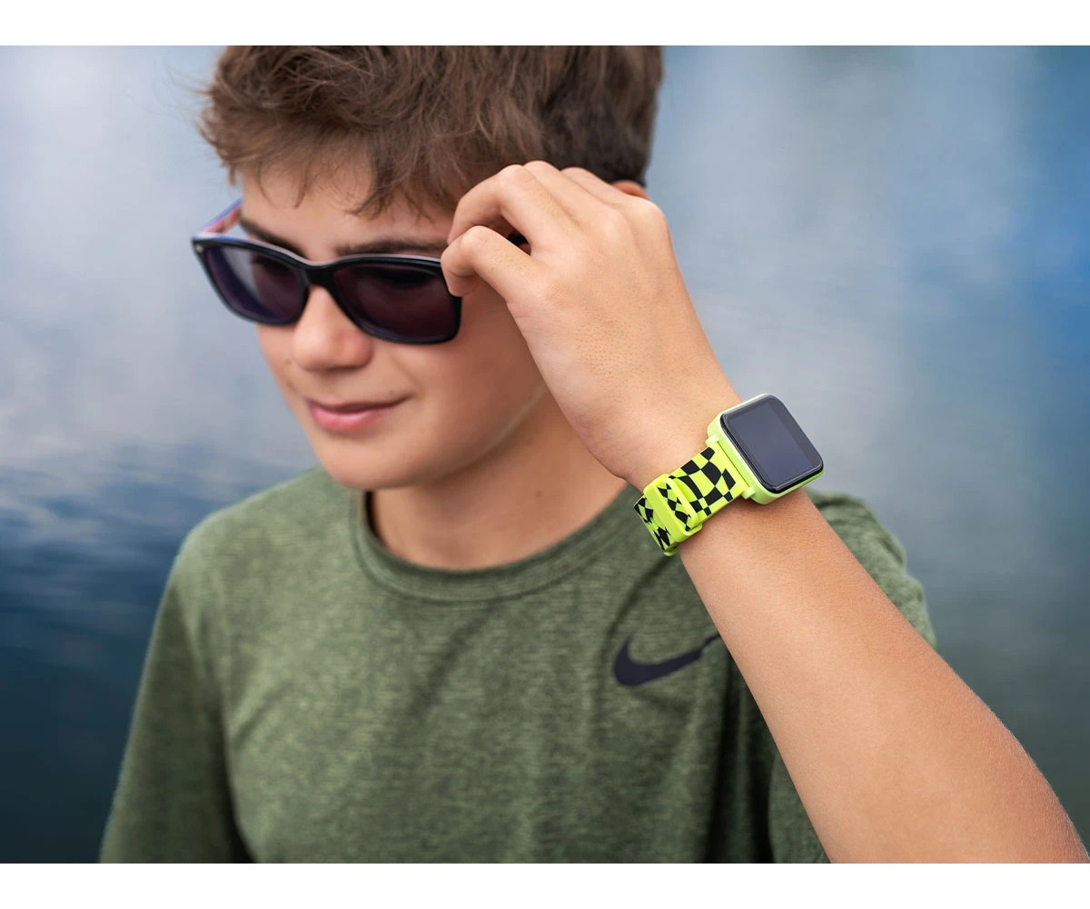 A boy in a green t-shirt and sunglasses wears a yellow and black smartwatch on his wrist.