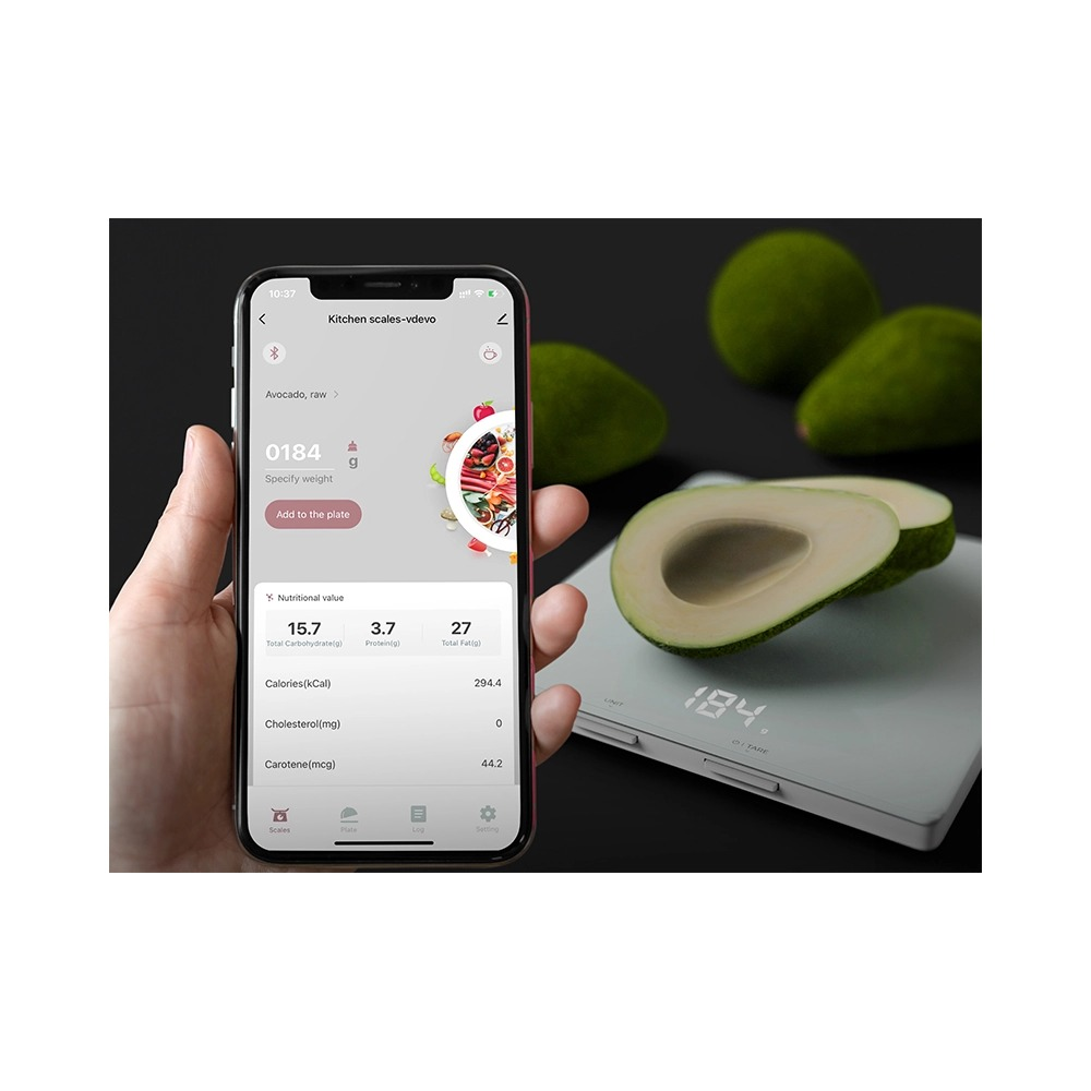 Ręka trzyma smartfon z aplikacją wagi kuchennej, z awokado i wagą w tle.