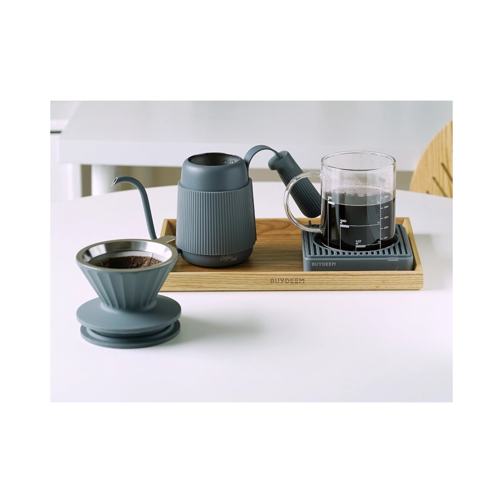 Un set per caffè filtro grigio con bollitore, tazza di vetro e dripper su vassoio di legno.