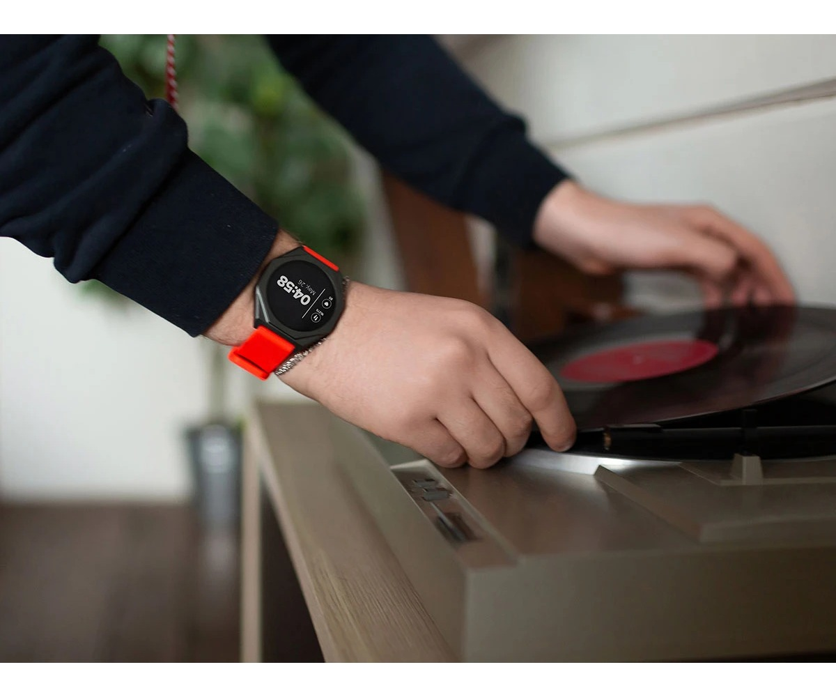 Osoba w smartwatchu z czerwonym paskiem kładzie płytę winylową.