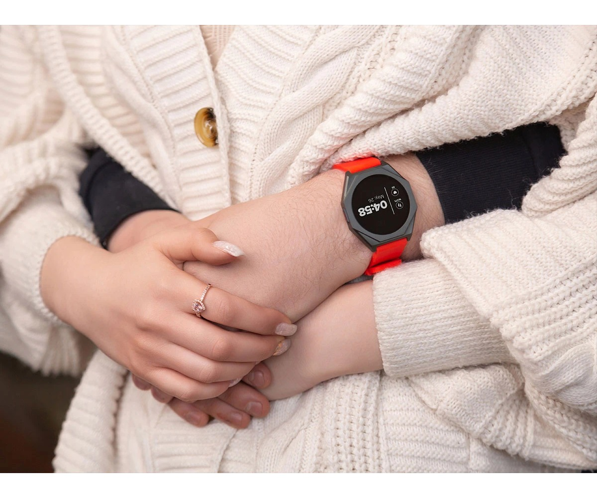Osoba ma na sobie czerwony smartwatch z okrągłym ekranem, podczas gdy inna osoba trzyma ją za rękę w ciepłym uścisk.