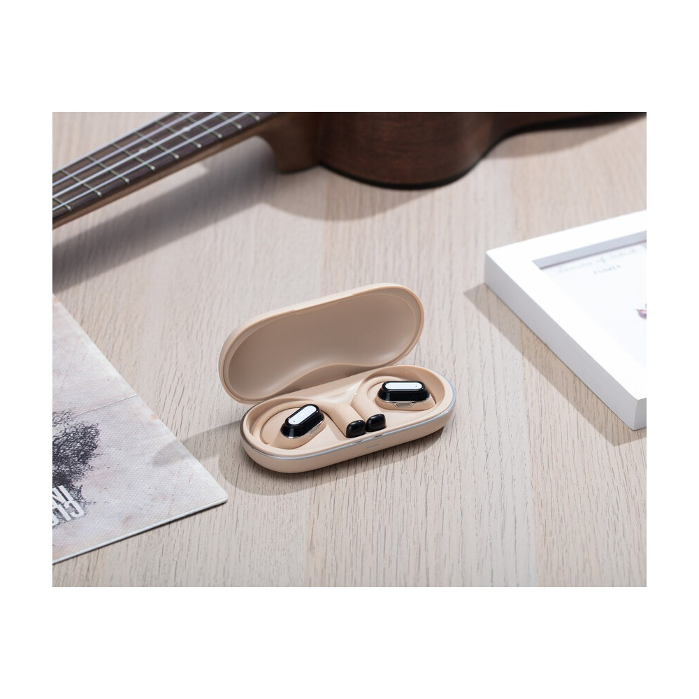 Beżowe słuchawki bezprzewodowe w etui ładującym na drewnianym stole z ukulele.