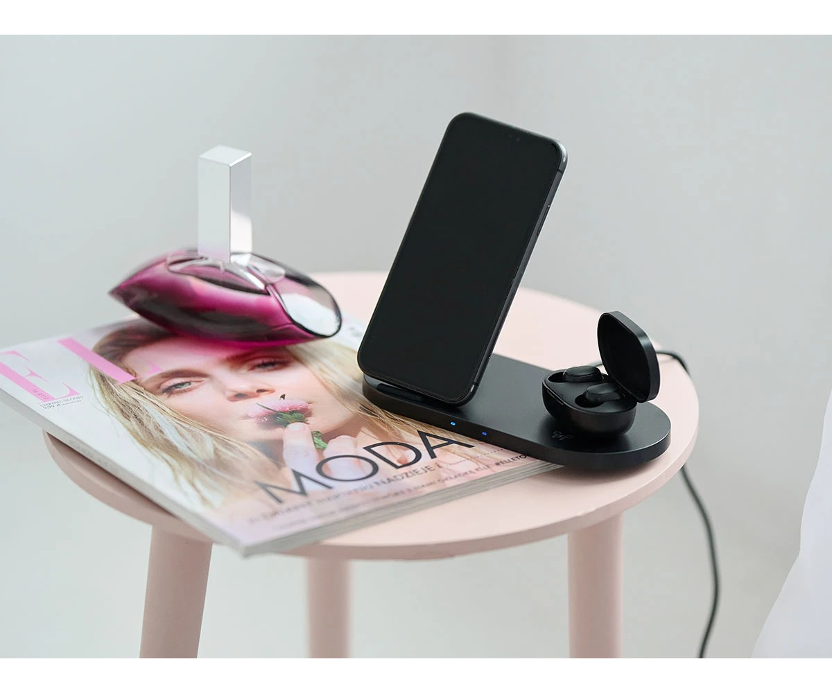 Smartfon i słuchawki na stacji ładującej, umieszczone na magazynie na małym okrągłym stoliku.