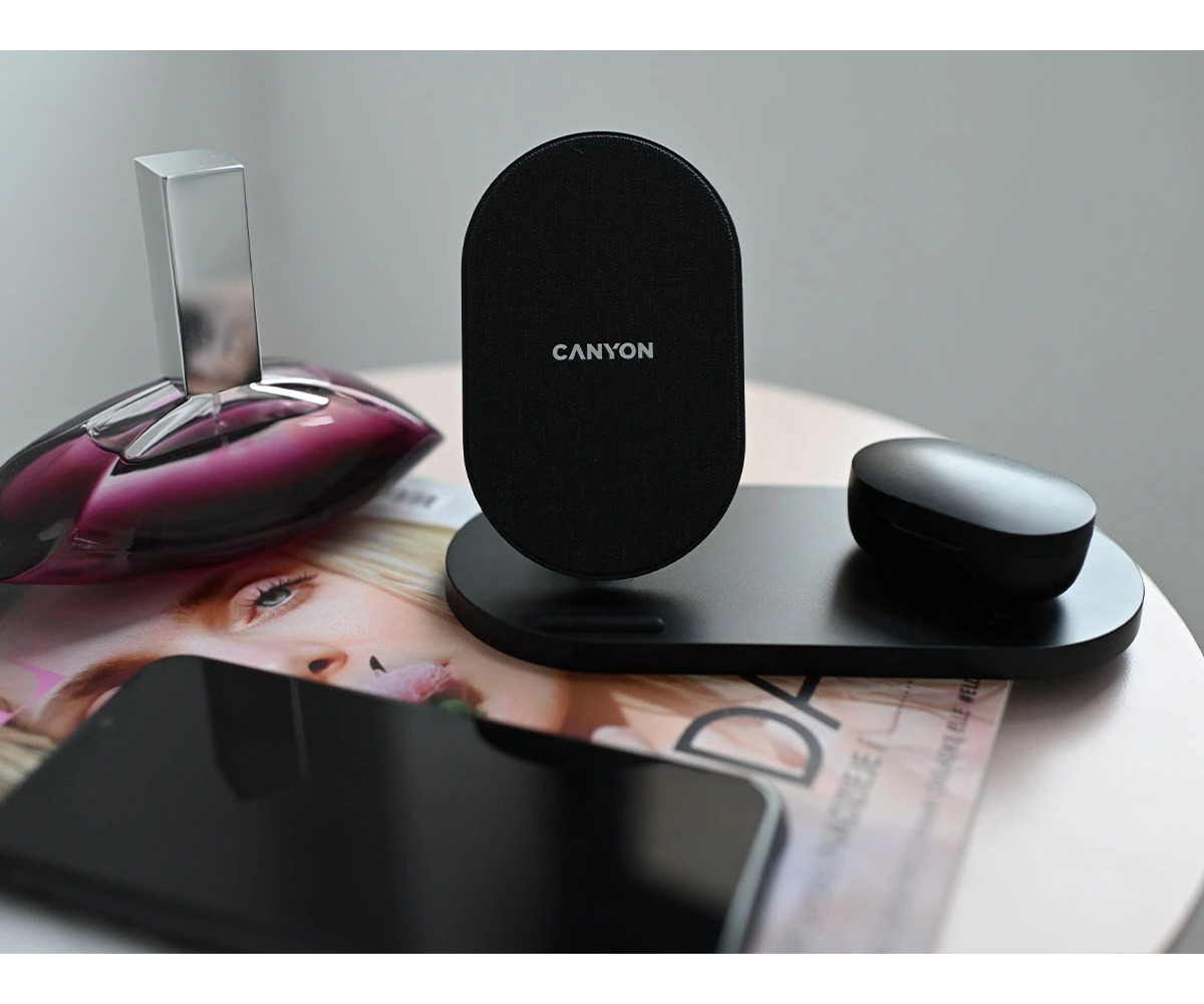 Czarna ładowarka Canyon, słuchawki douszne i smartfon na stole.