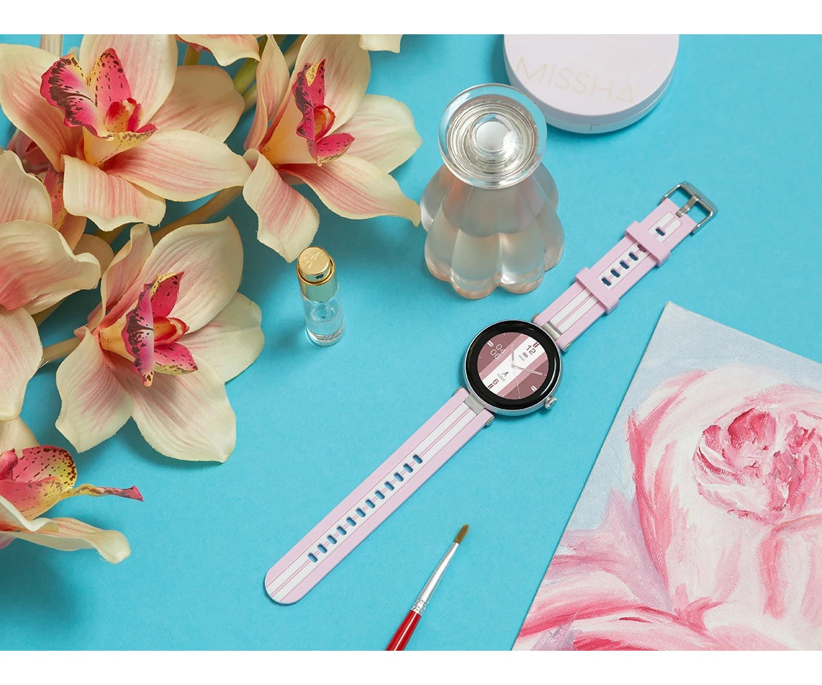 Różowy smartwatch, perfumy, orchidee i obraz na niebieskim tle.