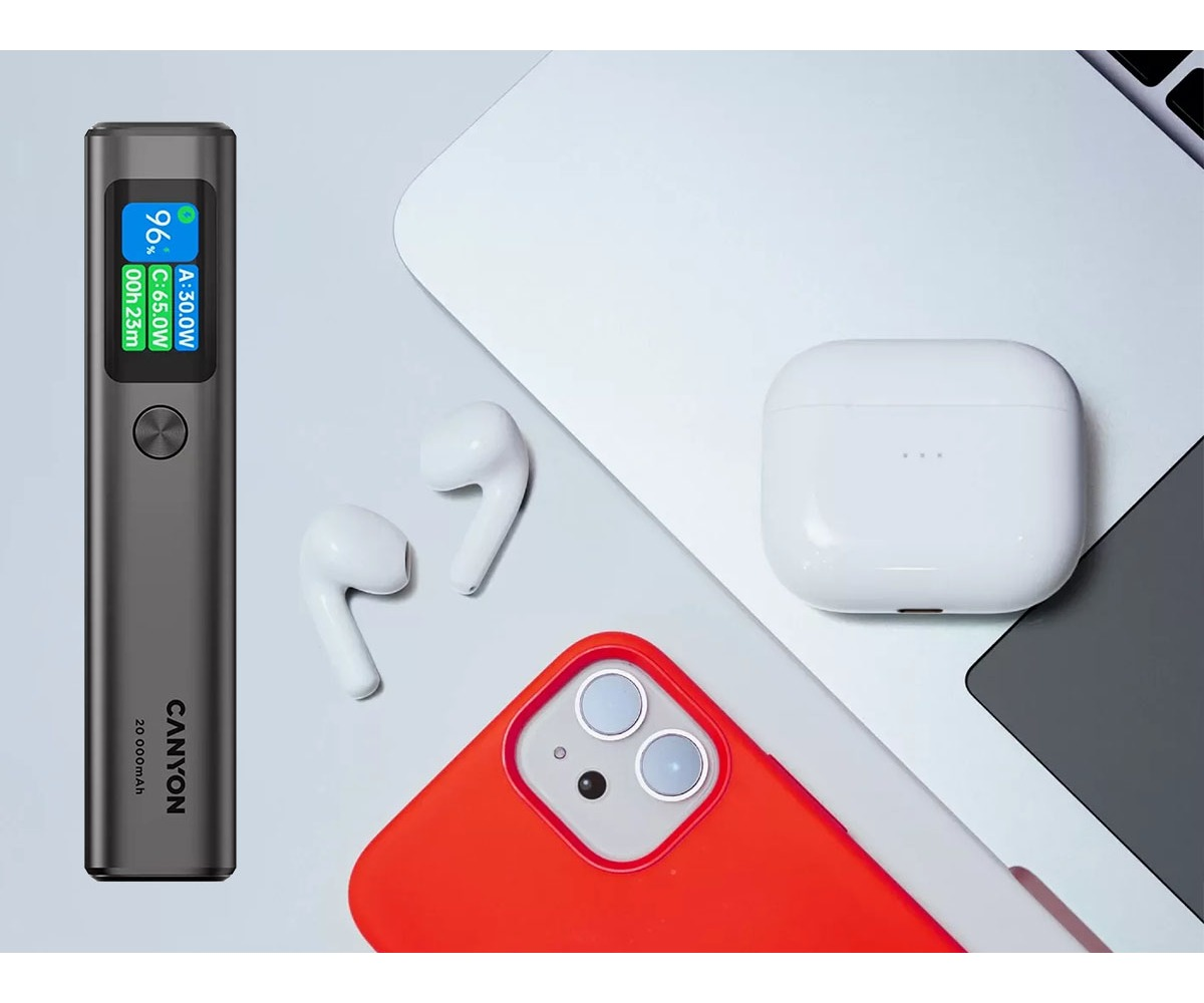 Powerbank, białe słuchawki, etui ładujące i czerwony telefon leżą na białym stole obok laptopa.