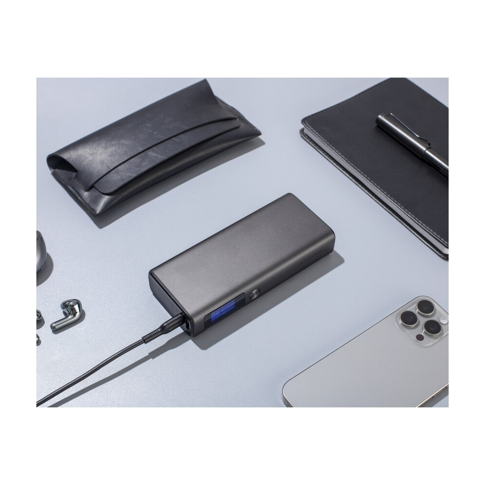 Powerbank z kablem leży na szarym biurku obok smartfona, notatnika, długopisu i słuchawek.