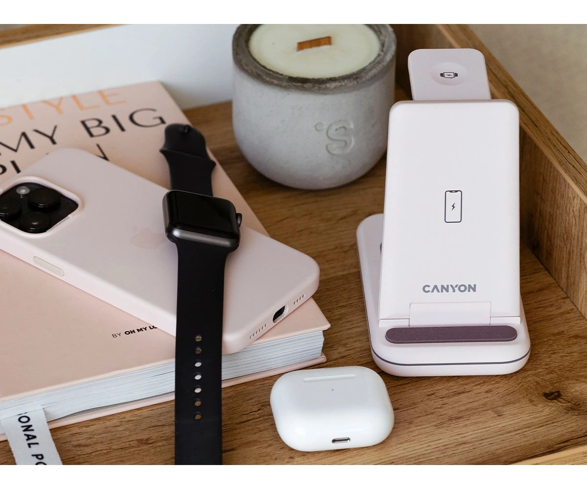 Różowy smartfon, smartwatch, słuchawki i stacja ładująca na drewnianym stole.