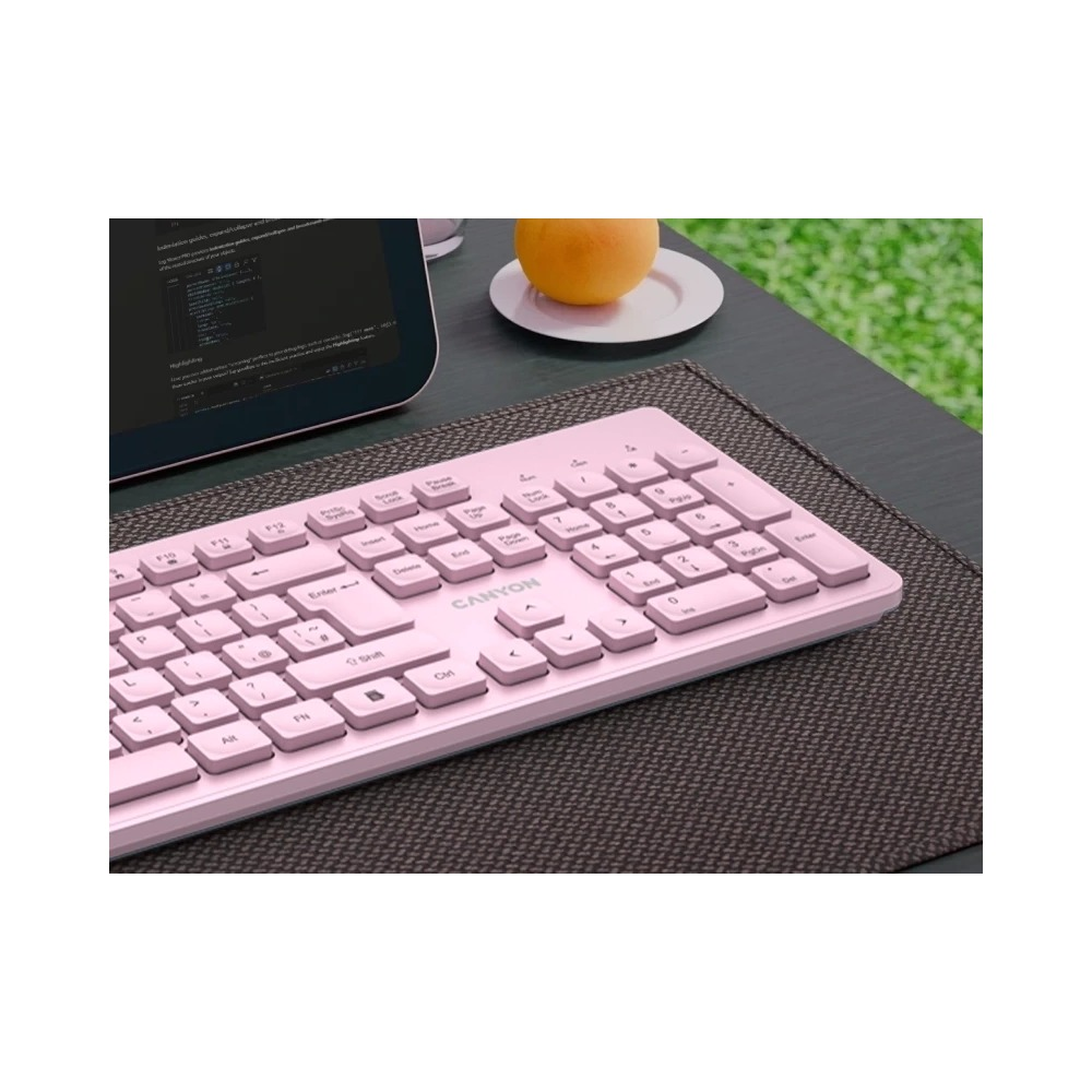 Różowa klawiatura Canyon na ciemnej podkładce, w tle tablet i pomarańcza.