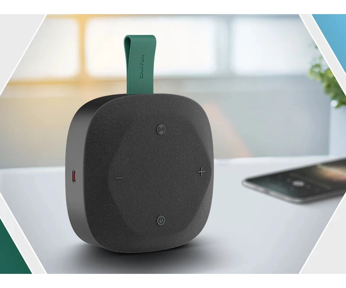 Przenośny szary głośnik bluetooth z zielonym paskiem do noszenia na stole.