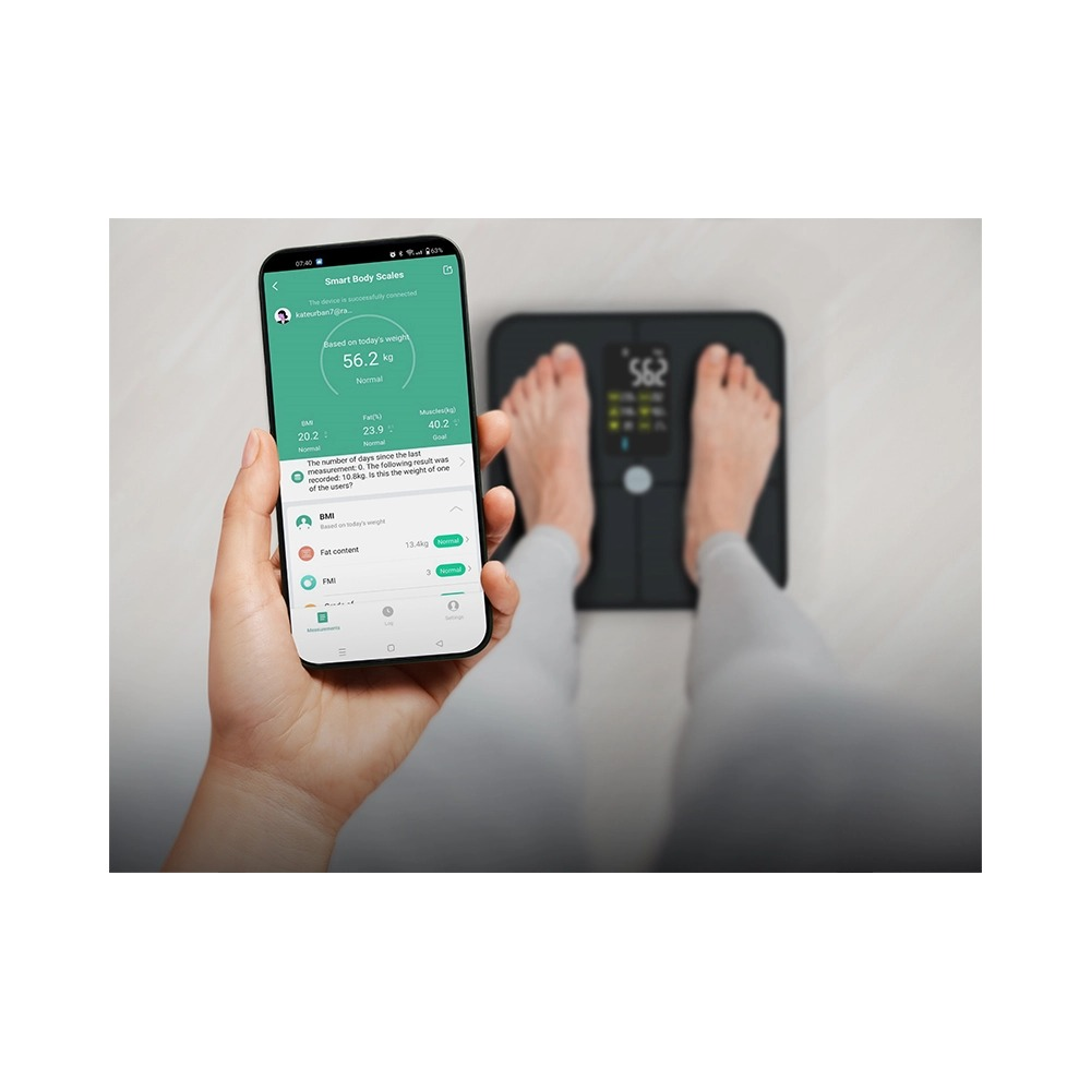 Osoba stoi na czarnej wadze i trzyma smartfon z aplikacją fitness.