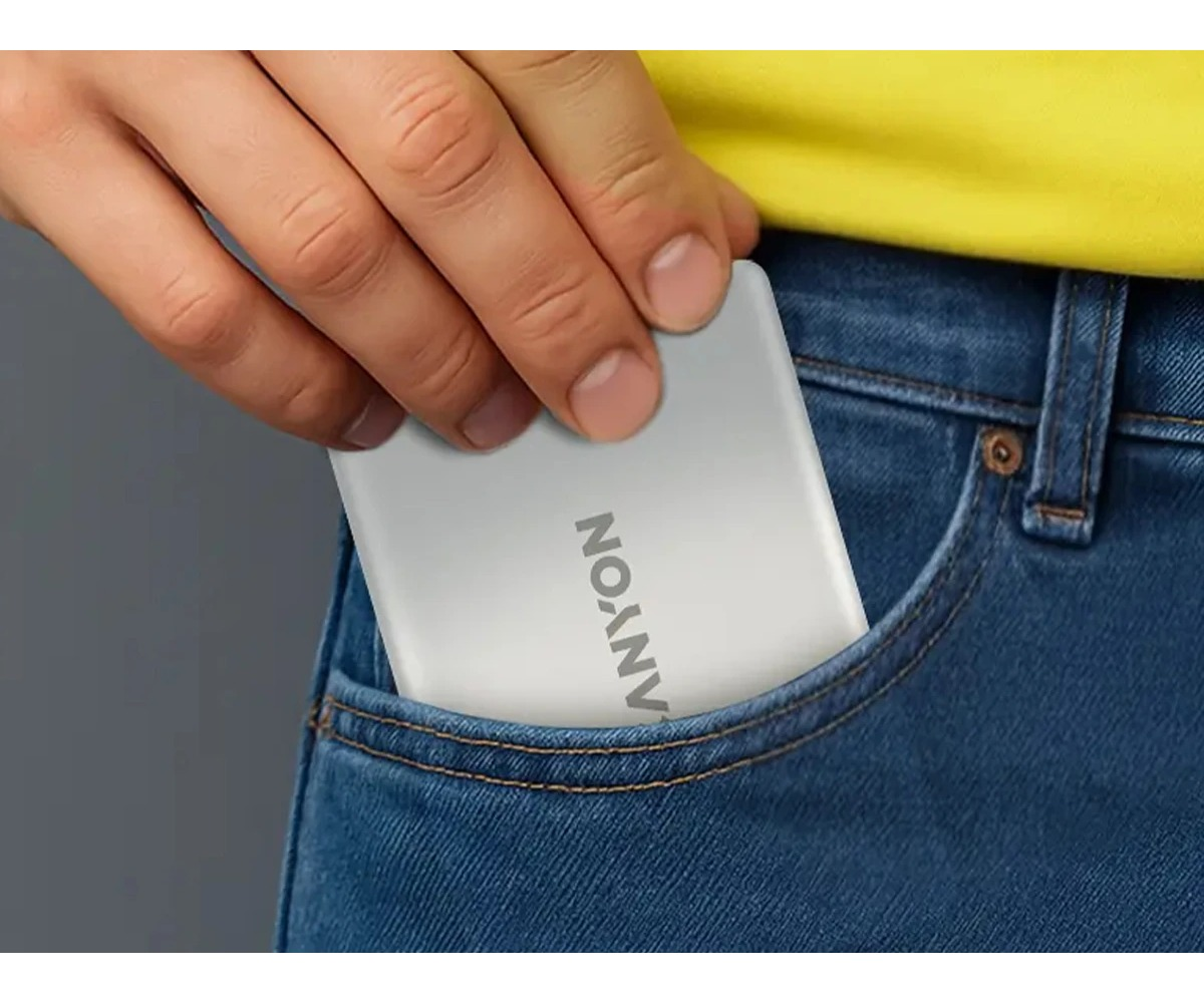 Ręka wkłada biały powerbank Canyon do kieszeni niebieskich dżinsów, w tle żółta koszulka.