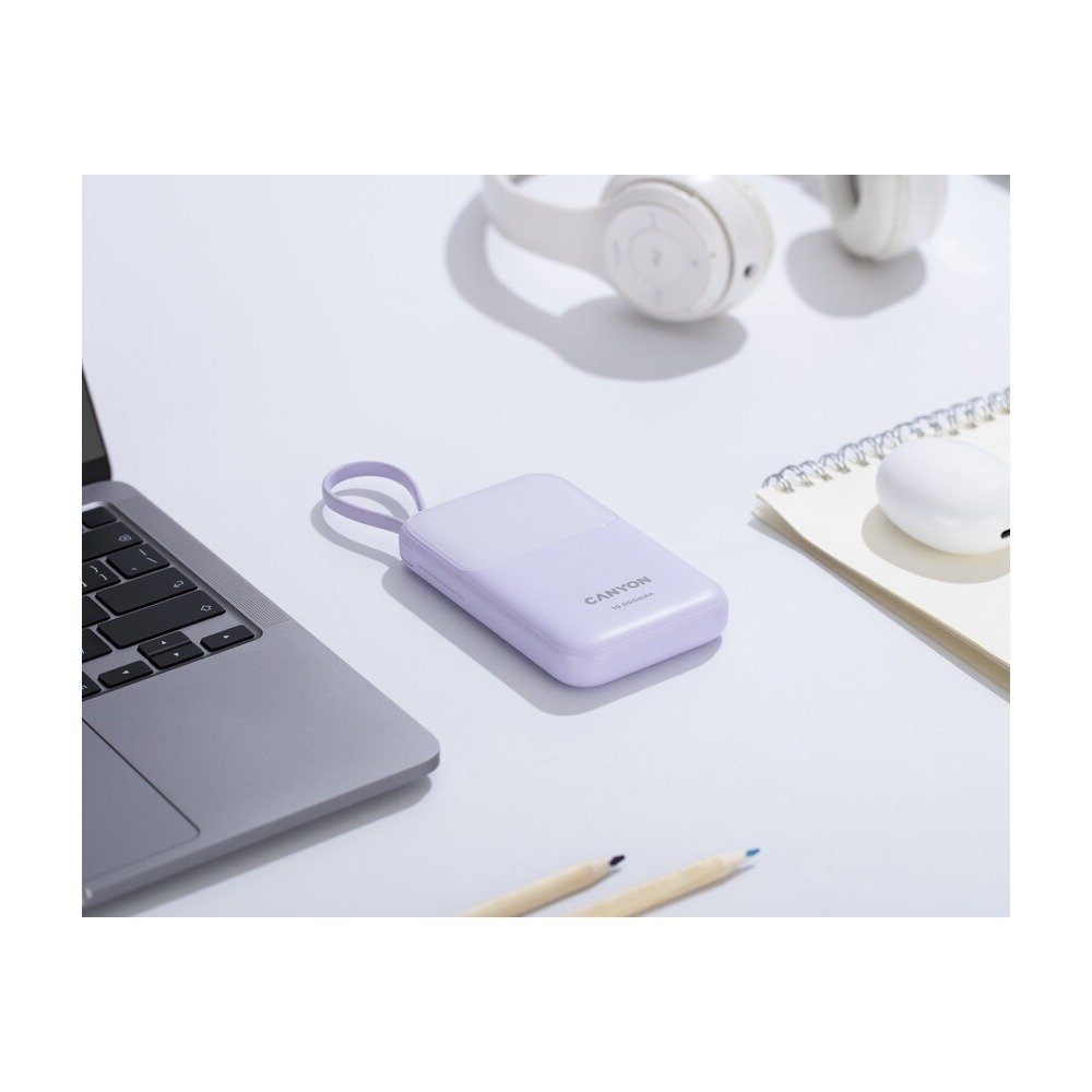 Fioletowy powerbank Canyon na jasnym biurku obok laptopa, słuchawek i notesu.