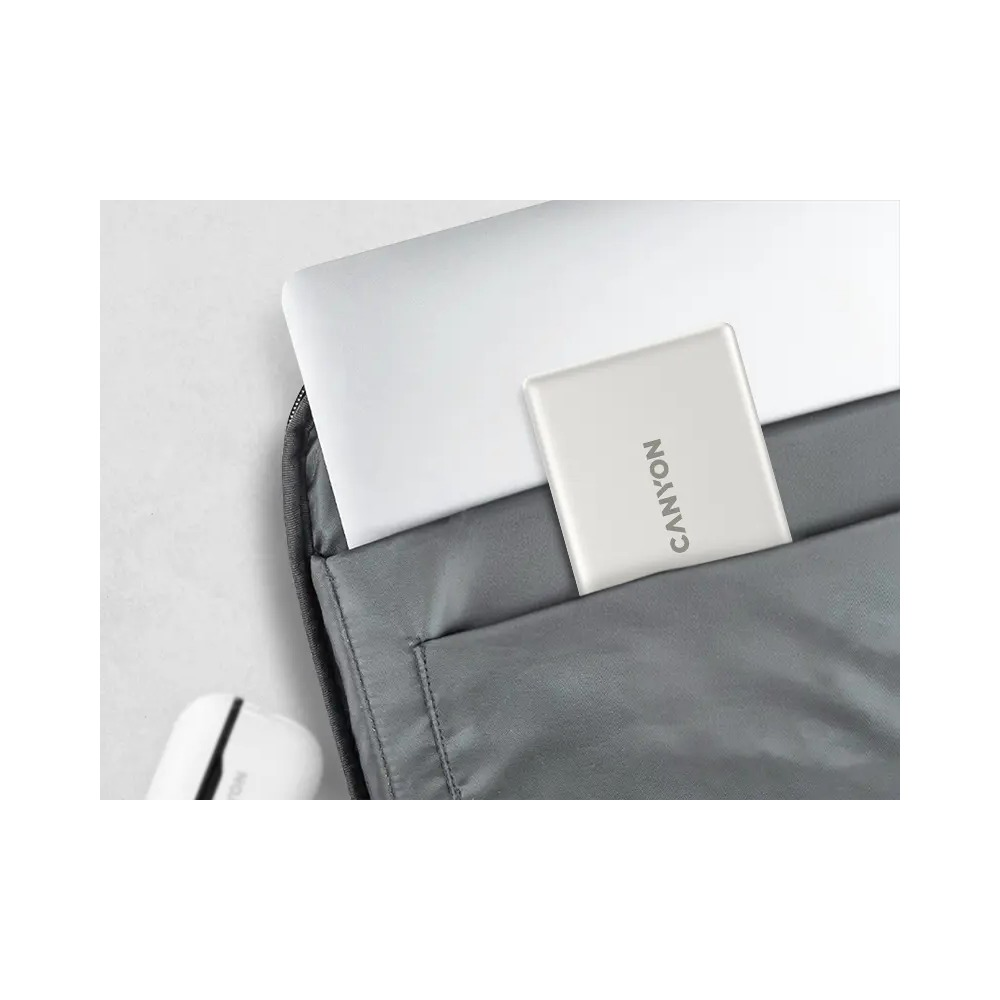 Srebrny powerbank Canyon i laptop są starannie umieszczone w szarym pokrowcu na jasnej powierzchni.
