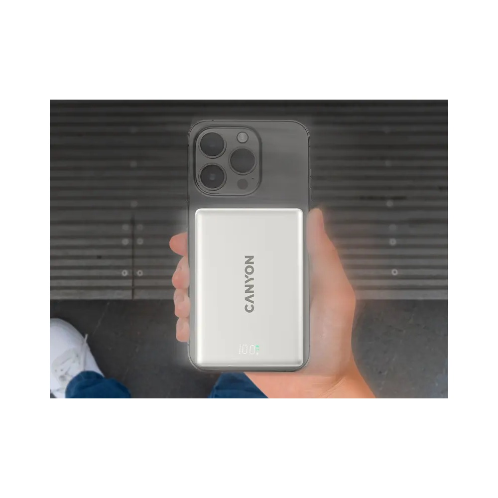 Ręka trzyma smartfon z dołączonym białym powerbankiem Canyon, wskazującym 100 procent.