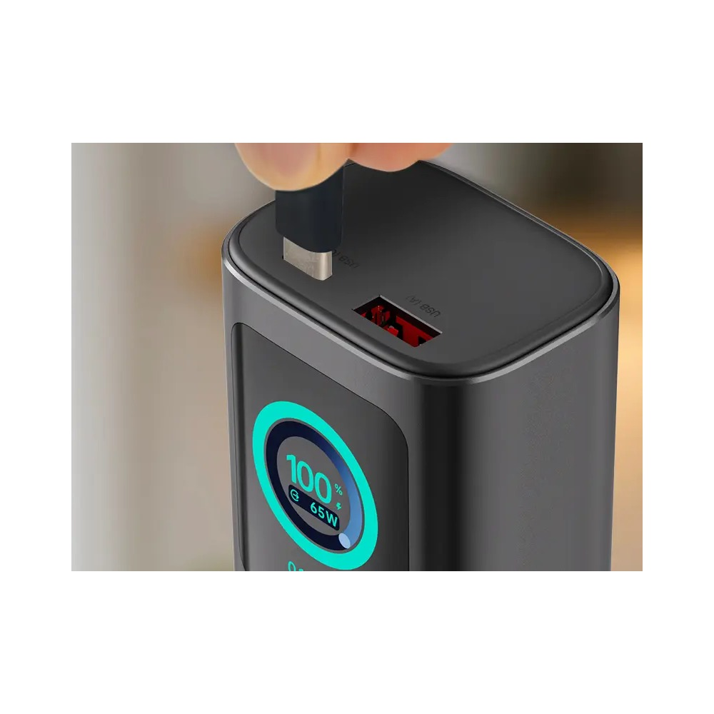 Ręka podłączająca kabel USB do szarego powerbanka z cyjanowym okrągłym wyświetlaczem pokazującym 100% i 65W.