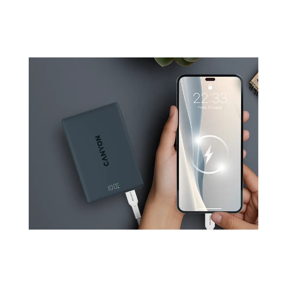 Ręka trzyma smartfon ładowany przez kabel z szarego powerbanku Canyon.