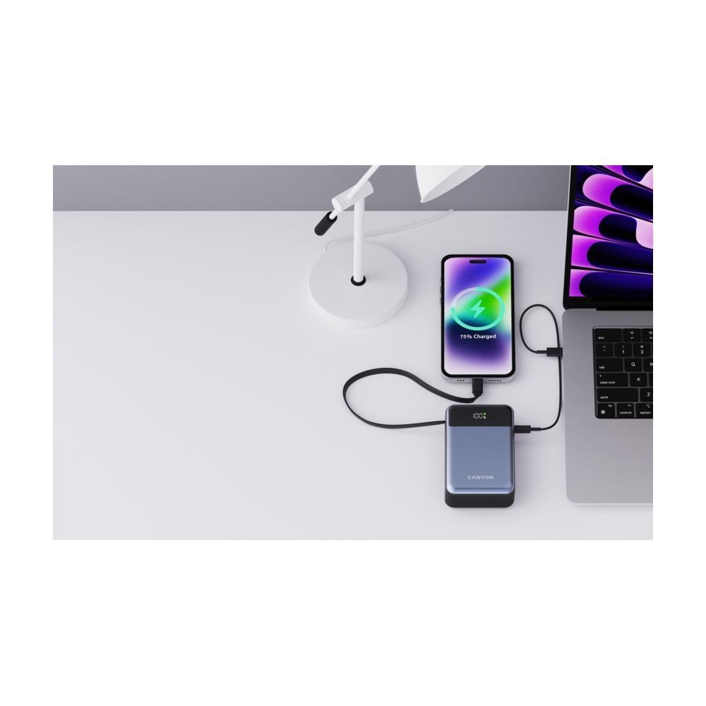 Smartfon, powerbank i laptop są połączone kablami na białym biurku obok lampy.