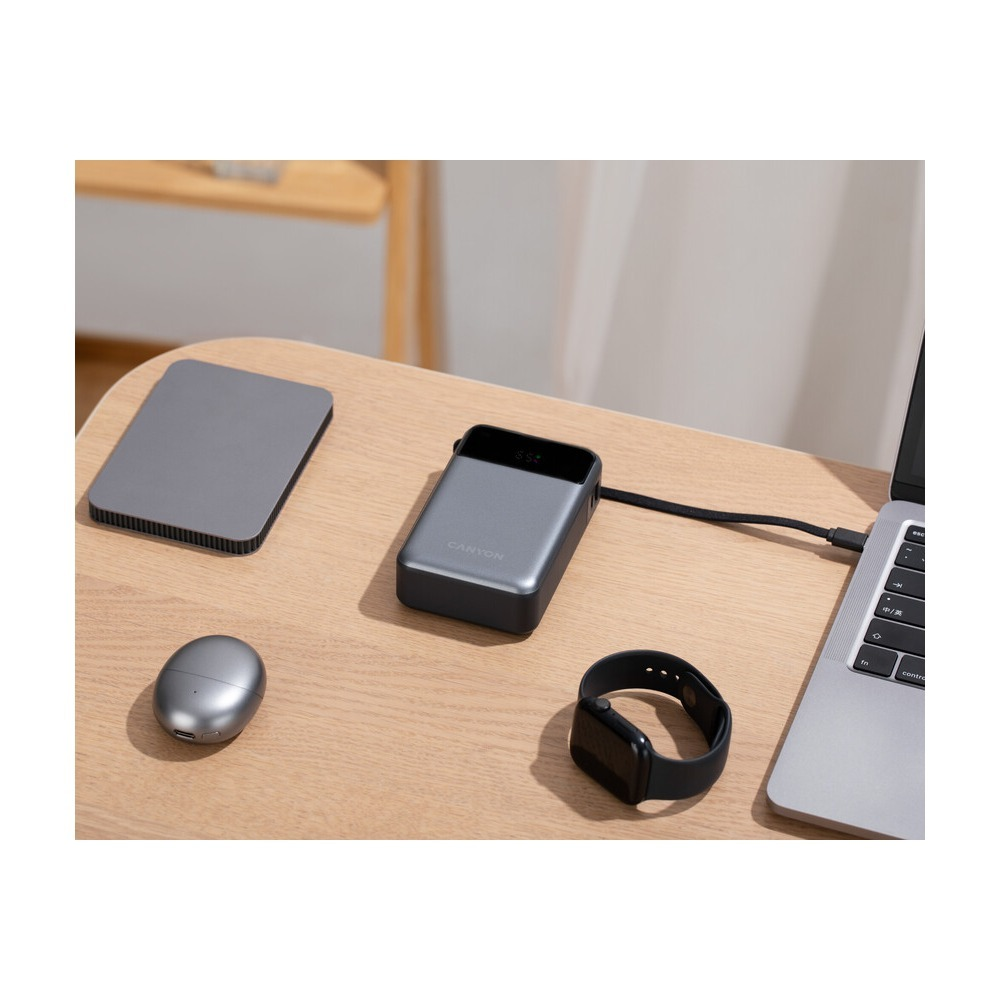 Powerbank, dysk, słuchawki, smartwatch i laptop leżą na drewnianym biurku.