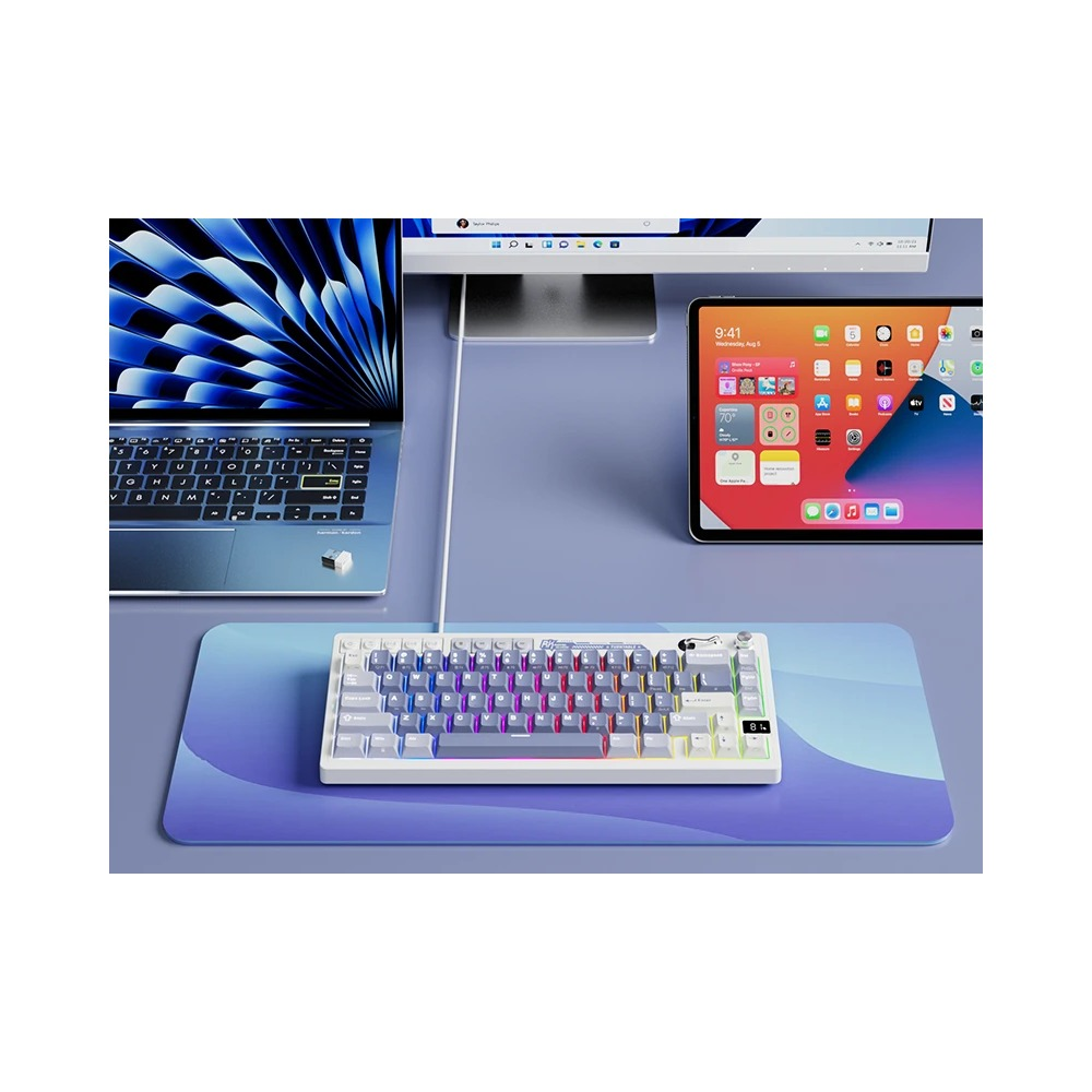 Podświetlana klawiatura na niebieskiej podkładce z laptopem, monitorem i tabletem.
