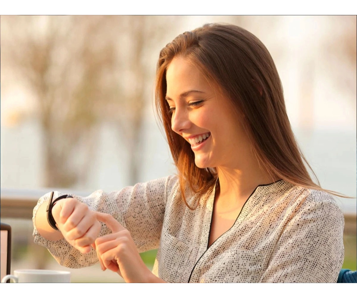 Uśmiechnięta kobieta w wzorzystej bluzce patrzy na swój smartwatch.