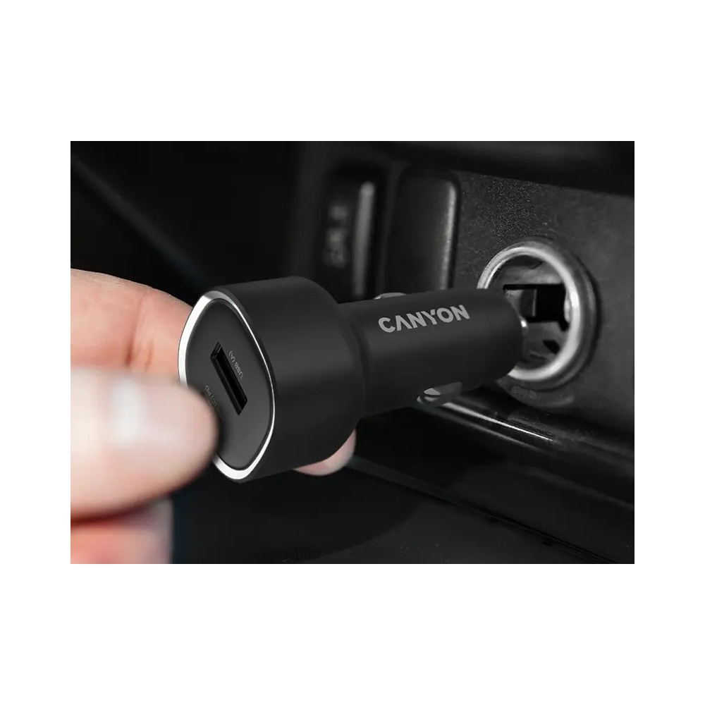 Ręka wsadza czarną ładowarkę samochodową USB Canyon do gniazdka.