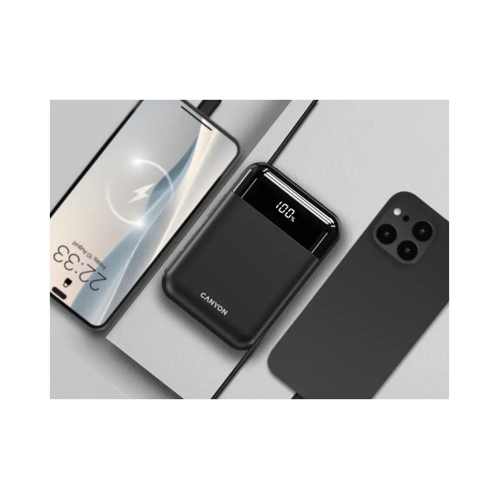 Powerbank z logo Canyon leży między dwoma smartfonami na szarej powierzchni.