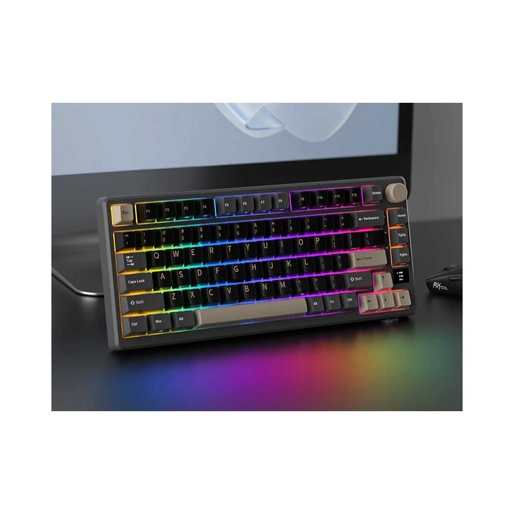 Un teclado negro compacto con retroiluminación RGB descansa en un escritorio oscuro frente a un monitor.
