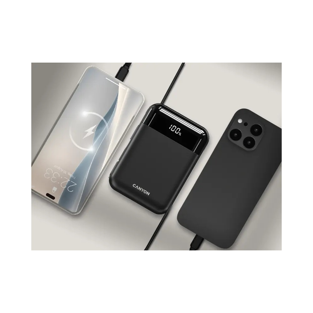 Czarny powerbank z wyświetlaczem LED 100% leży między dwoma smartfonami na neutralnym tle.