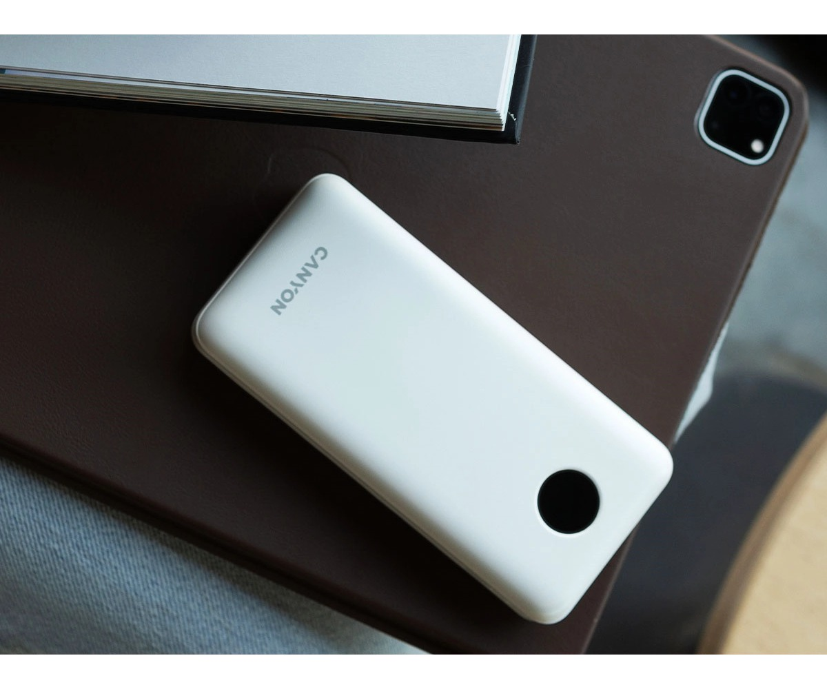 Biały powerbank Canyon na brązowym etui z notesem w tle.