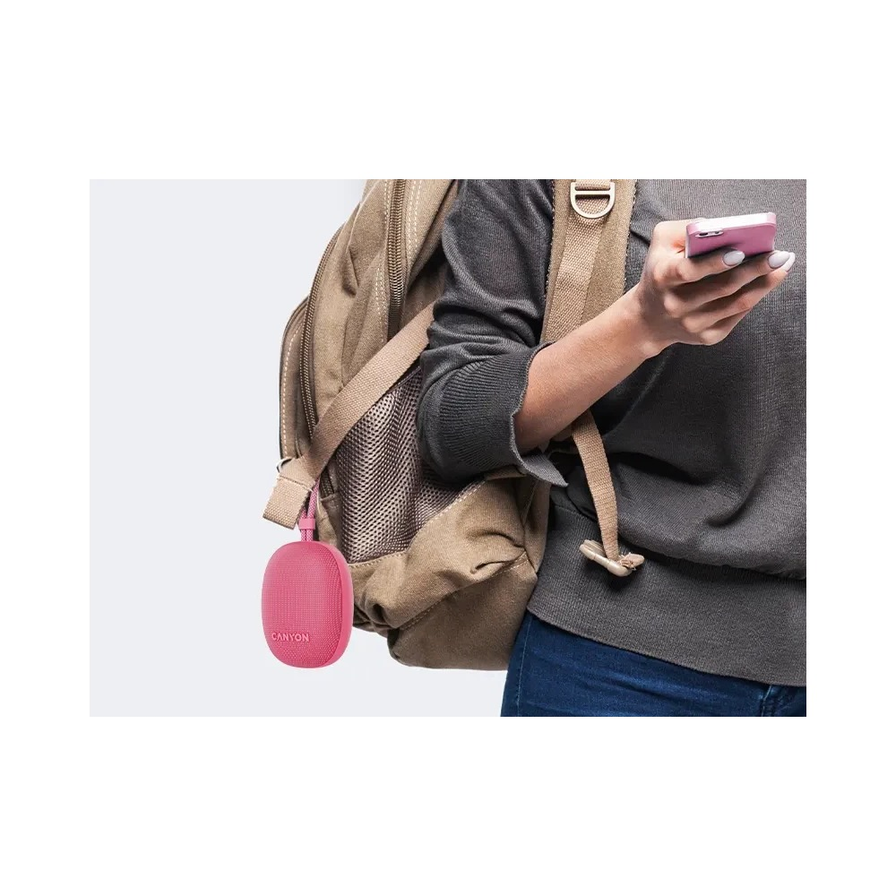 Kobieta z plecakiem trzyma różowy smartfon, a mały różowy głośnik wisi na plecaku.