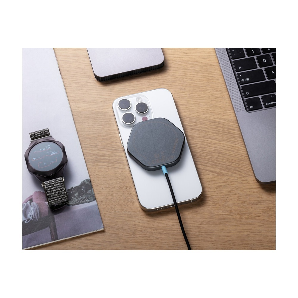 Biały smartfon z ładowarką MagSafe, smartwatch, laptop i notes leżą na drewnianym stole.