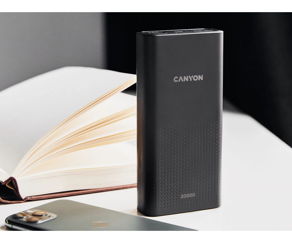 Czarny powerbank Canyon 20000 stoi na stole obok otwartego notesu i smartfona.