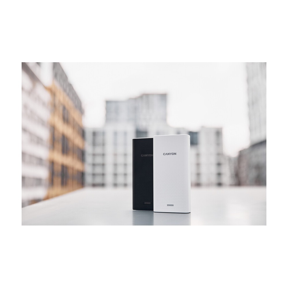 Biały i czarny powerbank Canyon 20000 stoją na powierzchni na tle rozmytego tła miasta.