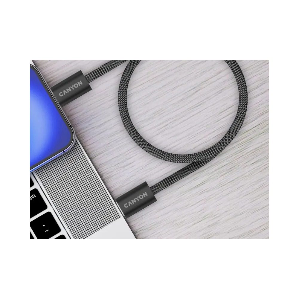 Czarny kabel Canyon podłączony do srebrnego laptopa na drewnianym blacie.