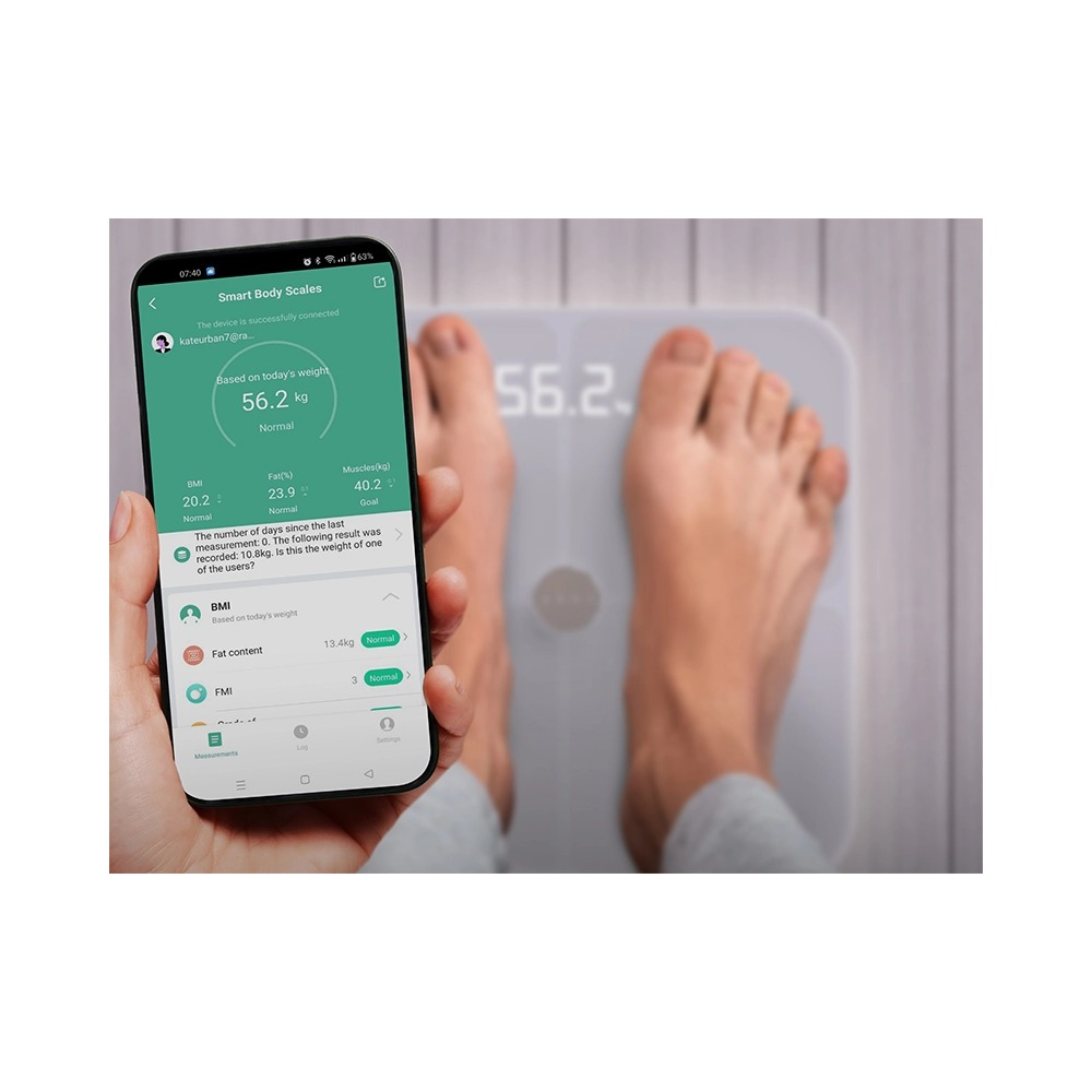 Osoba stoi na wadze, a smartfon wyświetla aplikację zdrowotną z pomiarami.