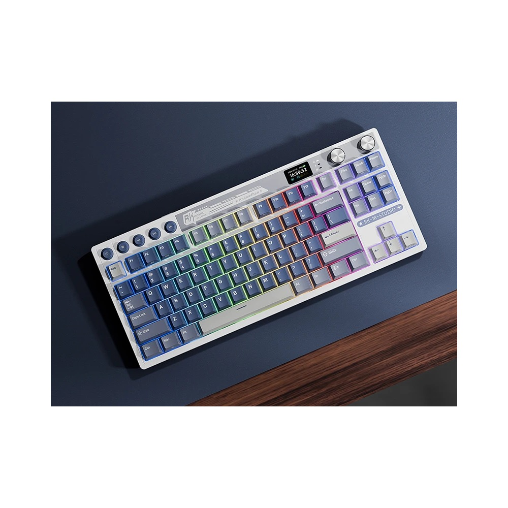 Biała klawiatura mechaniczna z podświetleniem RGB leży na niebieskim biurku obok drewna.